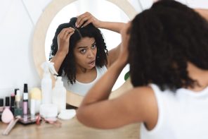 Black woman looking in the mirror at dandruff, dry scalp and flakes on her head